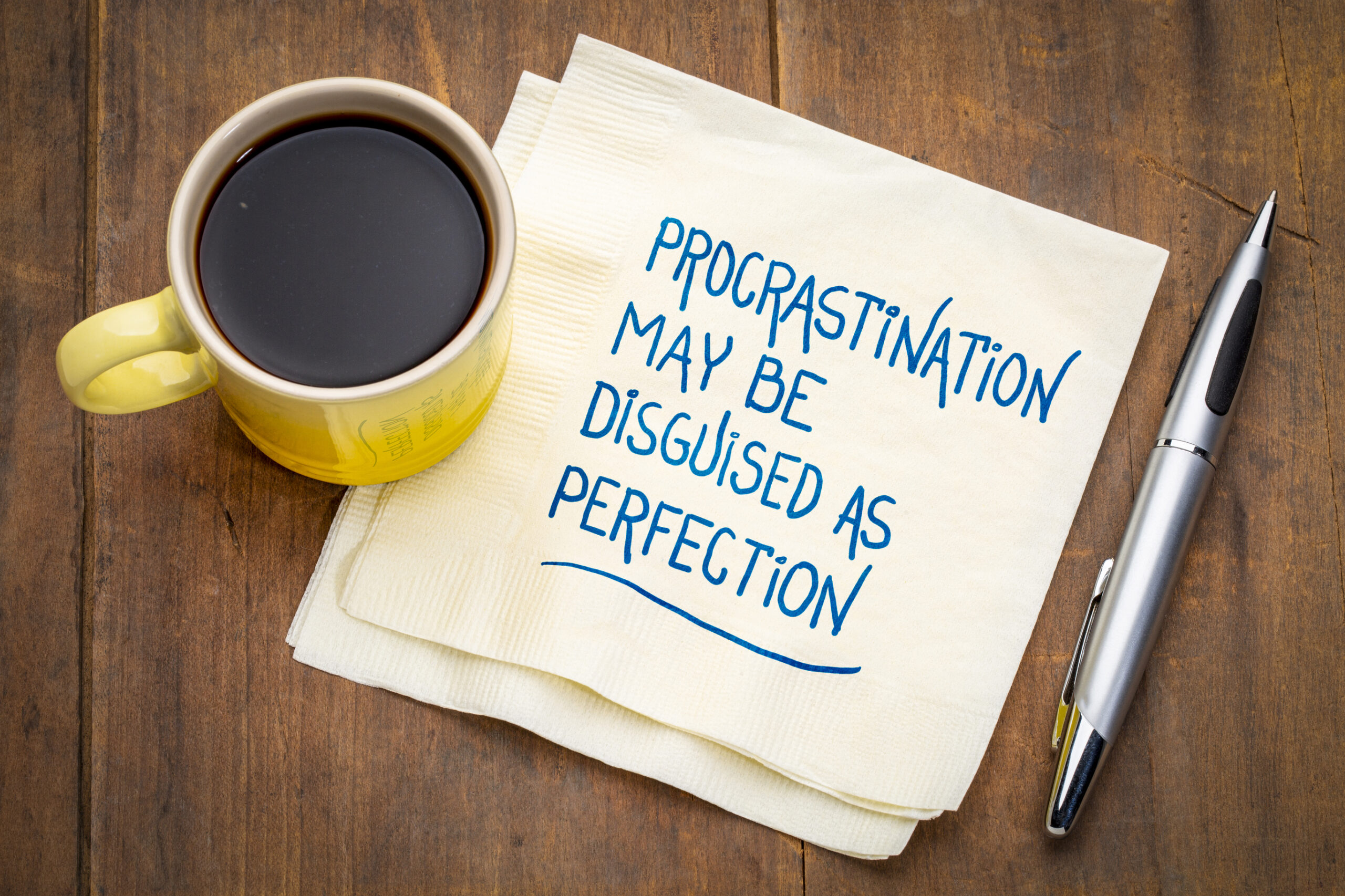 Coffe mug and a napkin that says procrastination may be disguised as perfection